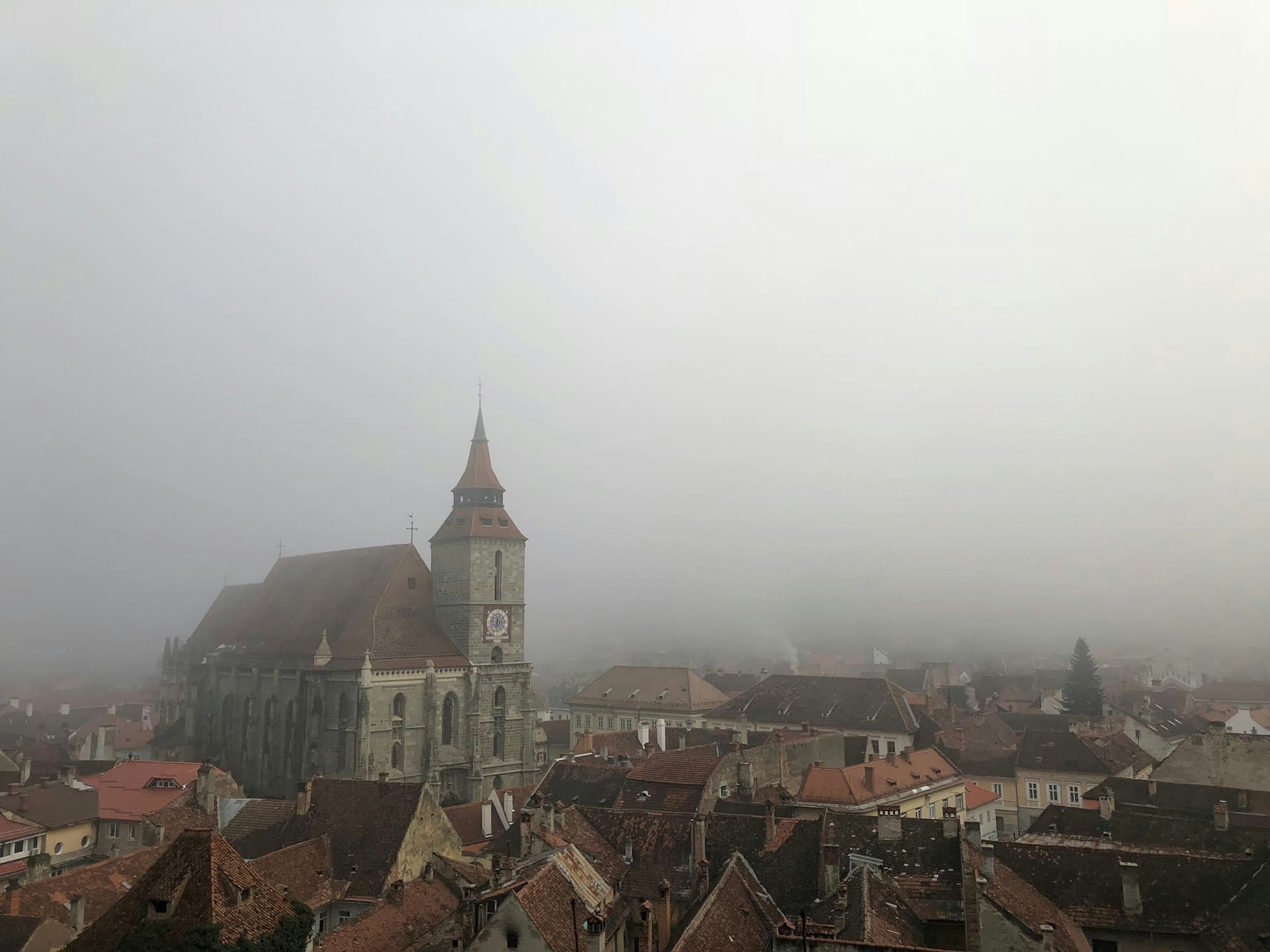 The Black Church tower rising above Brașov’s red roofs in morning fog