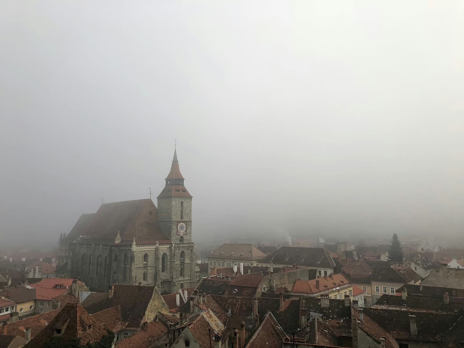 La torre della Chiesa Nera che svetta sopra i tetti rossi di Brașov nella nebbia mattutina