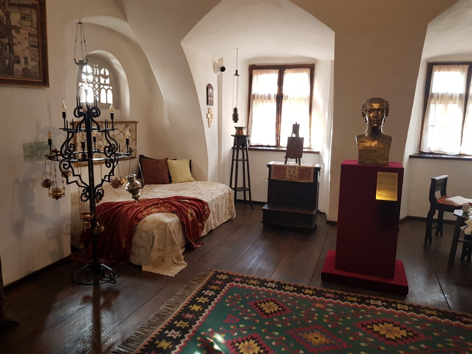 A furnished room inside Bran Castle with a bed, a bronze bust and a woven rug