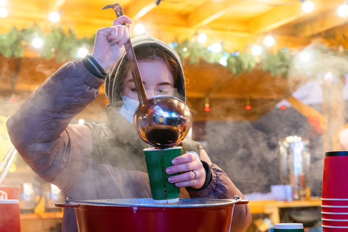 A stallholder ladles steaming mulled wine into a paper cup at a Christmas market