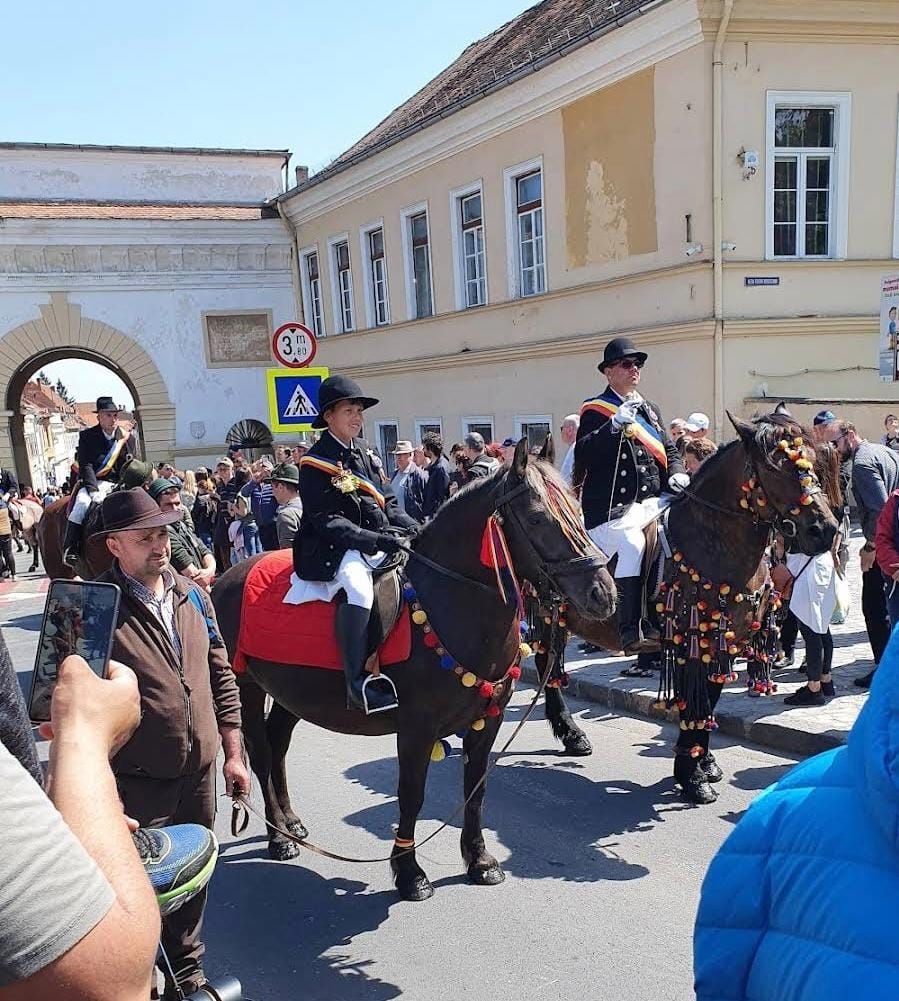 Un grup de călăreți Juni în costume tradiționale, purtând steaguri.