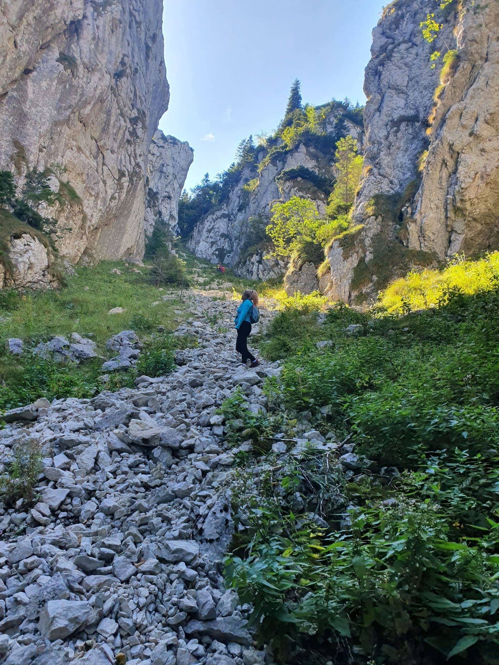 A hiker on a rocky trail between limestone cliffs in Piatra Craiului