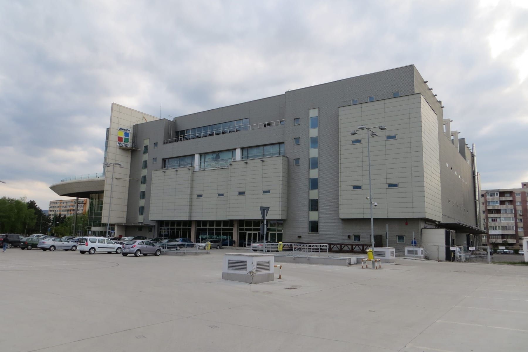 Il grande edificio grigio e squadrato dell'Unirea Shopping Center con il logo colorato, visto da un ampio parcheggio